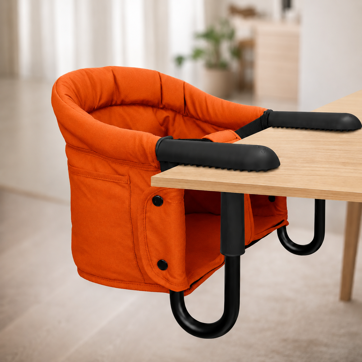 Orange baby chair with black armrests attached to a wooden table.
