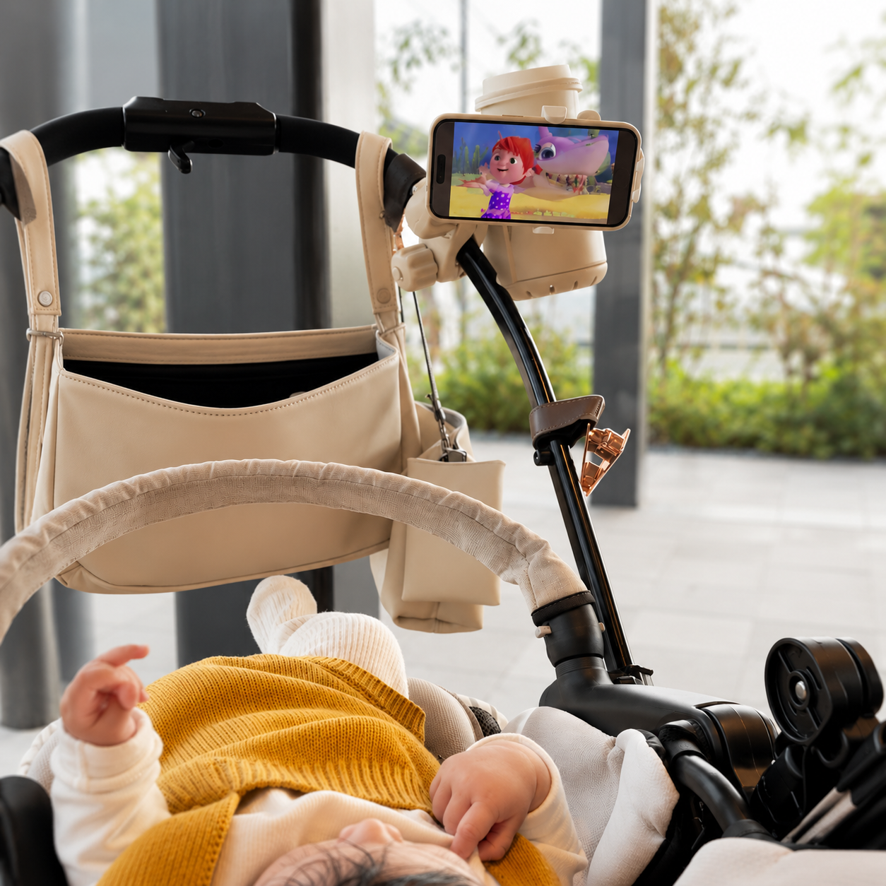 Baby in a stroller with a smartphone holder displaying a cartoon on a screen.
