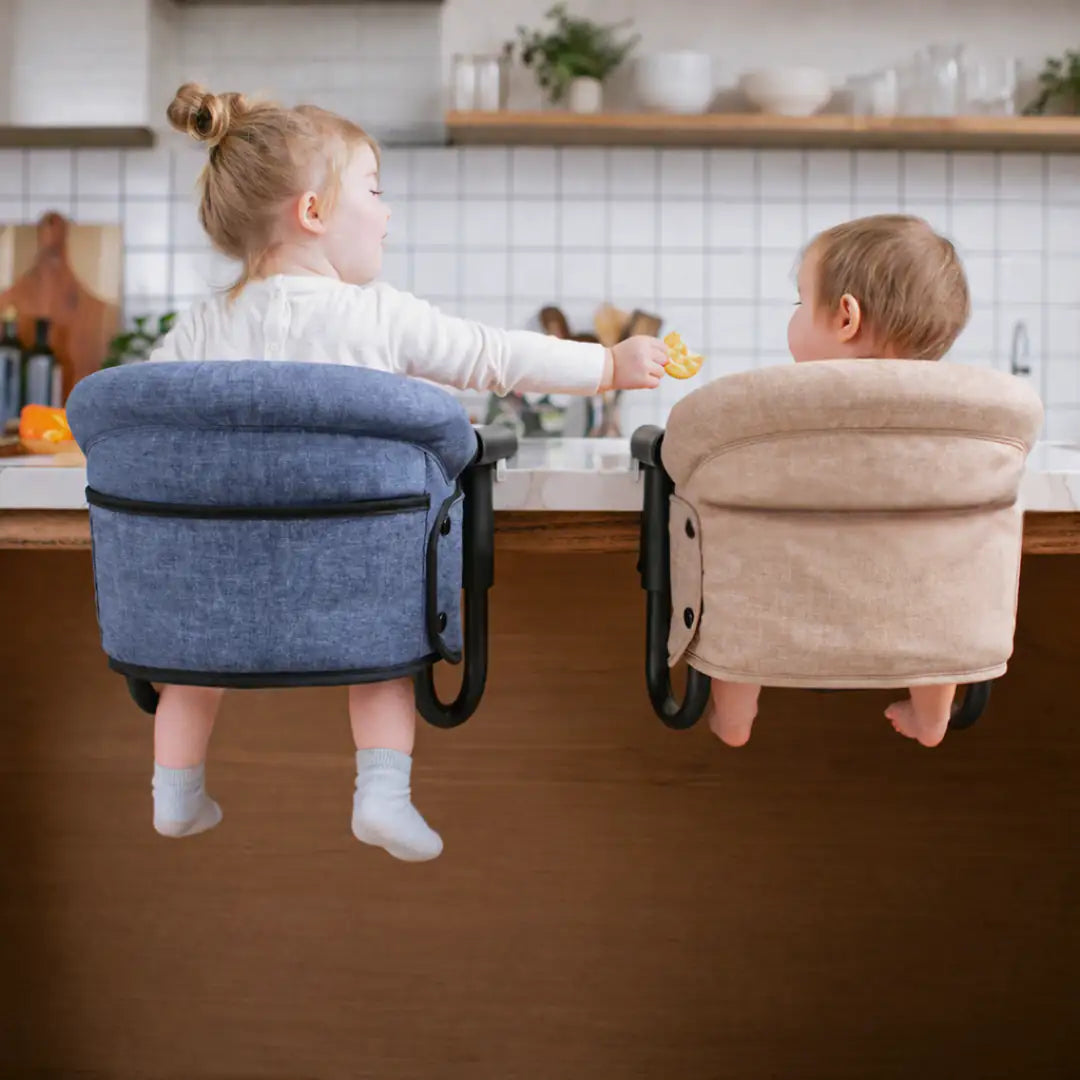 Two children sitting in portable high chairs at a kitchen counter.